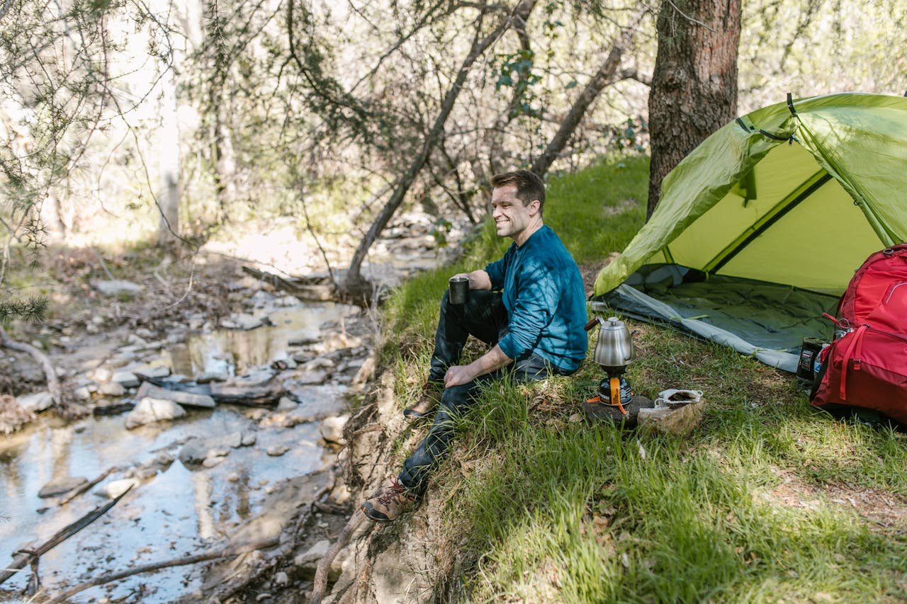 Man in Blue Jacket Sitting Beside Green Tent